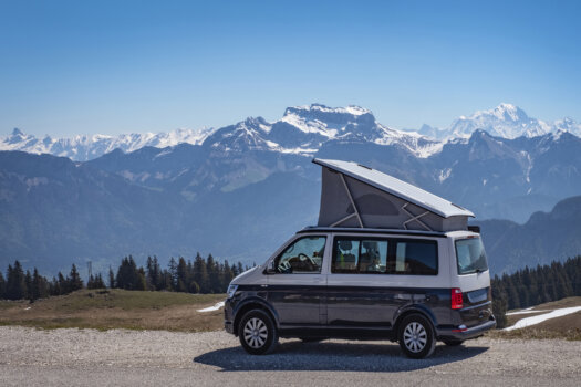 Ein VW Bus Campervan mit Aufbaudach vor einer schönen Bergkulisse.